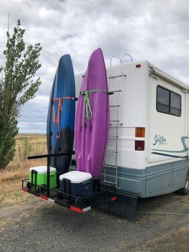 Kayaks mounted on the back of an RV with coolers, set against a cloudy sky.