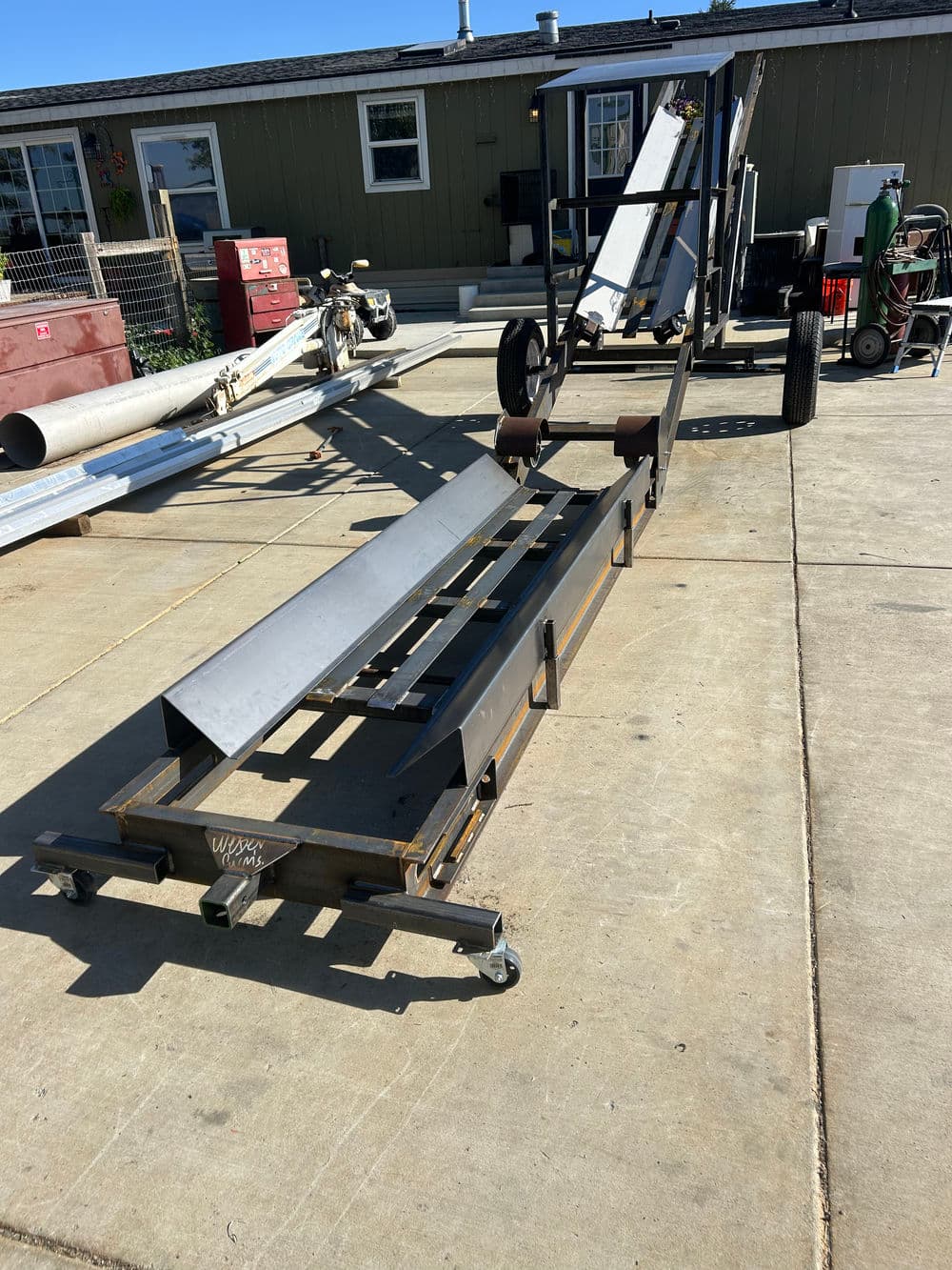 Metal conveyor system on wheels in a workshop with industrial equipment and storage.