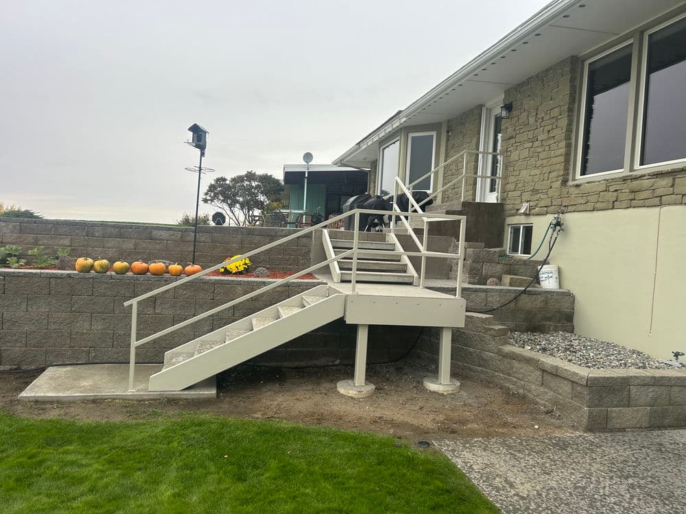 Exterior view of a house with a ramp and stairs, pumpkins in the garden, and gray stone walls.
