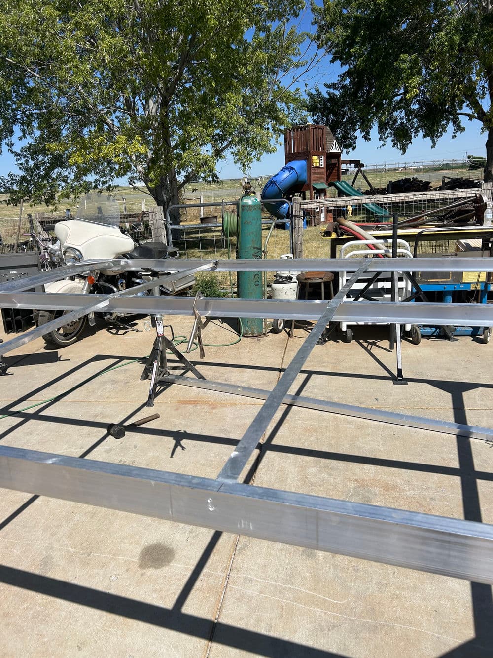 Metal framework on concrete with green tanks and farm equipment in a rural setting.